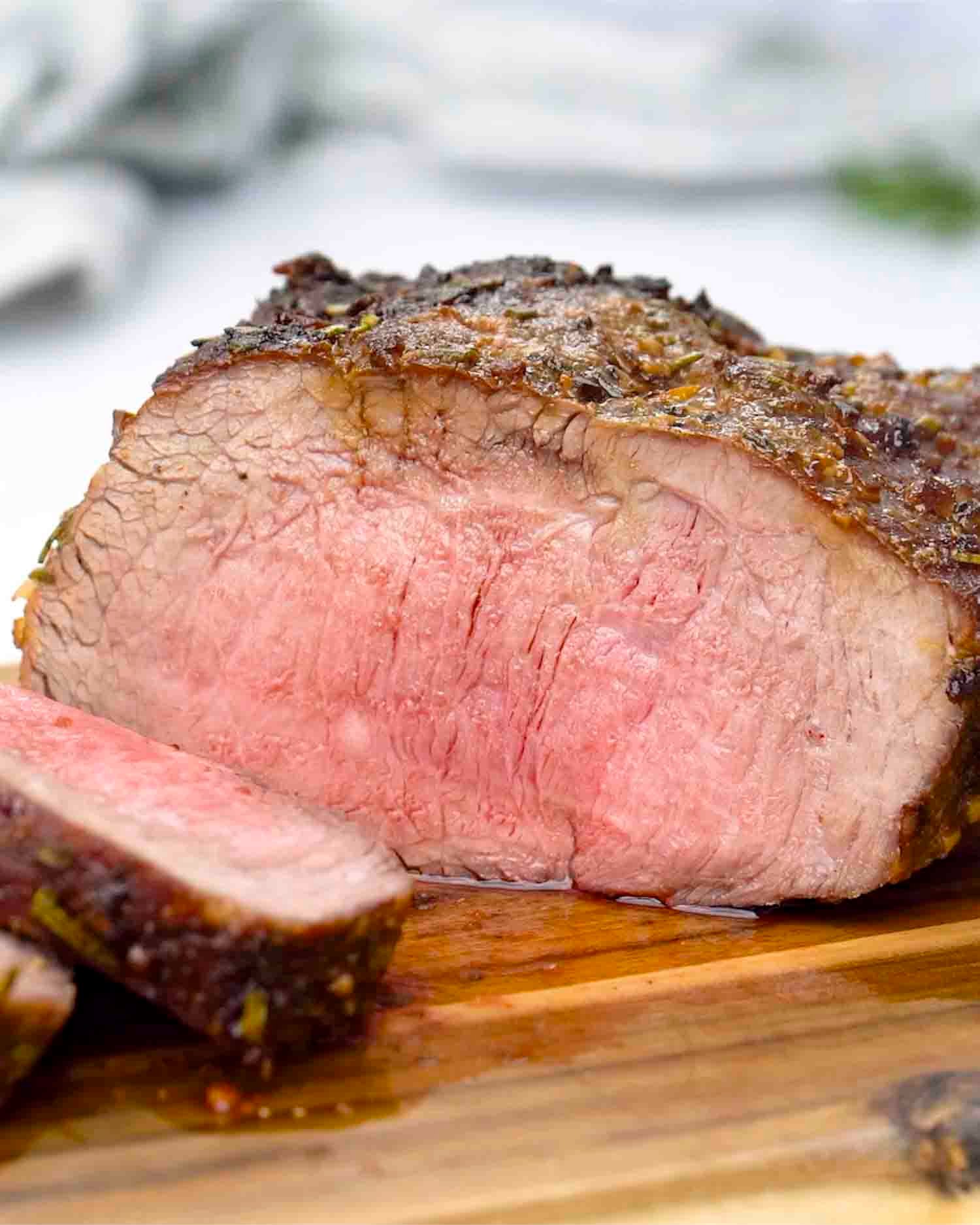 a roast beef made in the air fryer sliced on a cutting board.
