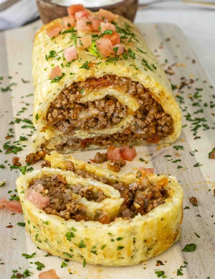 a beef potato roll on a cutting board cut into slices and garnished with parsley.